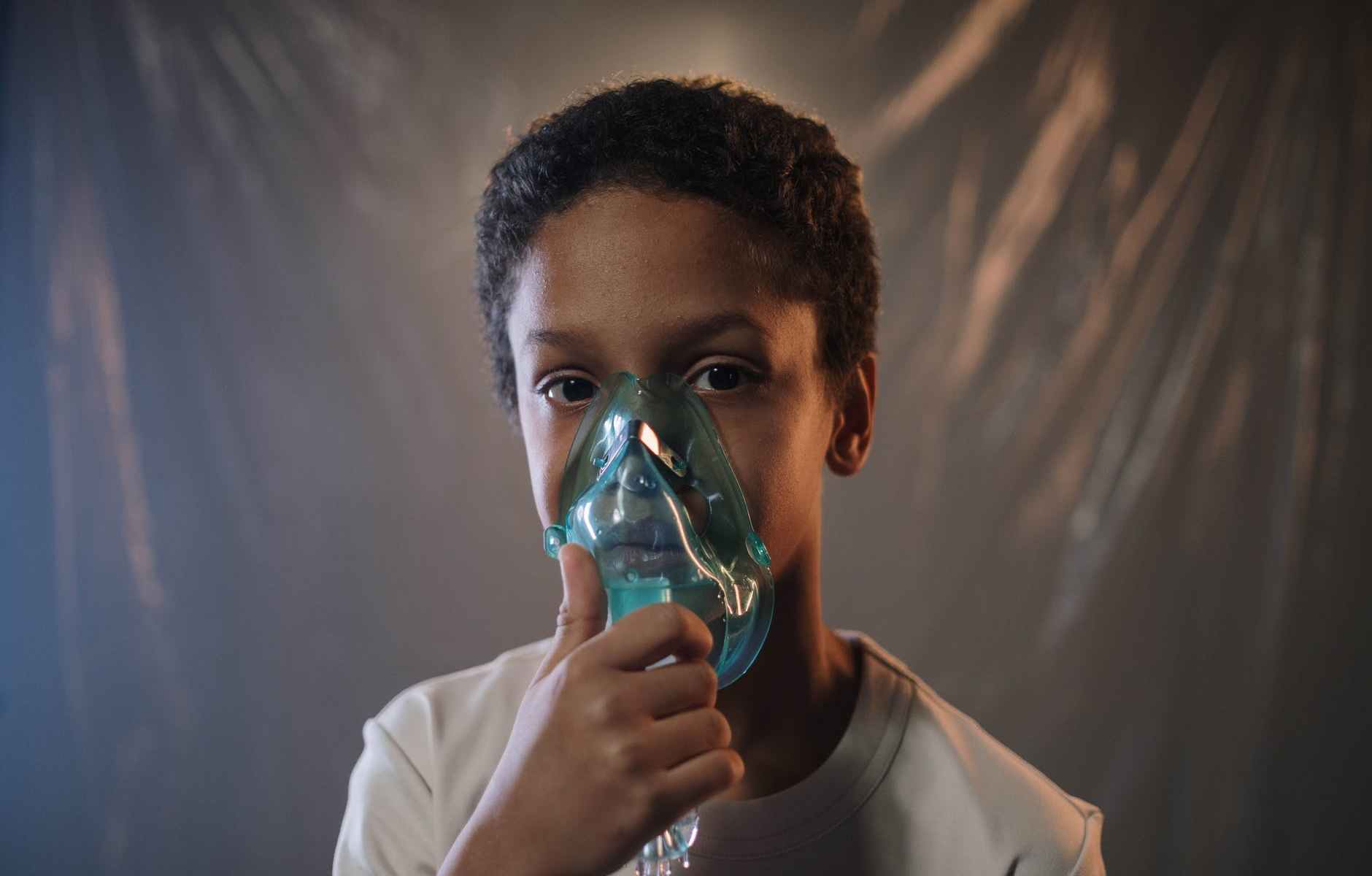 a boy in white shirt holding green oxygen mask